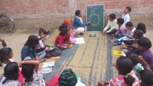 VLC-Lokipur-me-ganit-catch-up-se-ghari-dekhana-batate-huye Children seated together during a Village Learning Center session